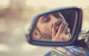 man yawning in car mirror