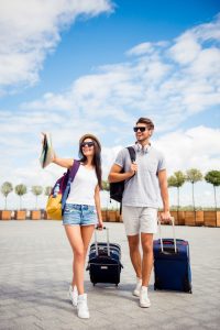 couple taking selfie while pulling suitcases behind them